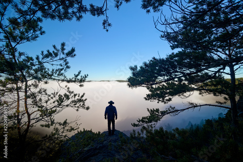 Silhouette of a solitary man among the trees above a misty valley.