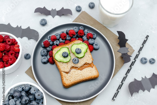Funny scary monster on halloween sandwich toast bread with peanut butter,blueberry,raspberry,bats.Kids child sweet dessert breakfast lunch food on gray background close up.