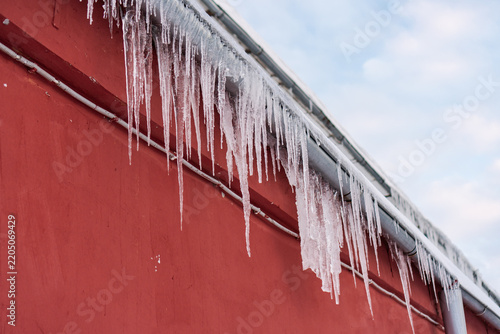 A red building with a metal gutter is covered in long, thick icicles along the roof edge.