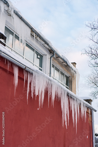 Winter weather conditions concept. Icicle danger in cities concept. Photo of multiple icicles formed on the roof of house.