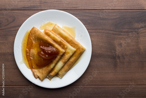 Top view photo of crepes, thin pancakes, British pancakes with apple jam on the white plate on wooden table with copy space.