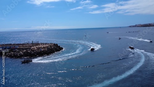 Vista con dron de lanchas rápidas dejando estelas blancas en el Atlántico azul junto al rompeolas de un puerto, Costa Adeje, Tenerife, Islas Canarias