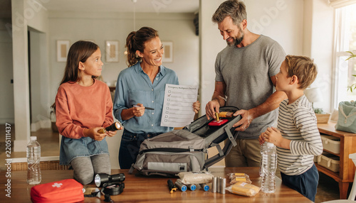 A smiling family works together at home to organize an emergency backpack, using a checklist to ensure readiness. This heartwarming scene promotes safety, preparedness, and responsible teamwork.