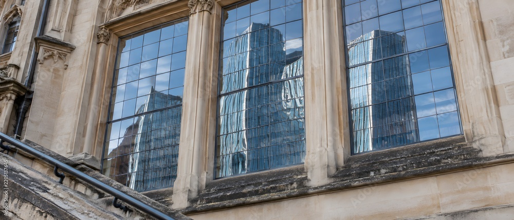 Obraz premium Mirrored slab of modern glass tower warped across Victorian library windows