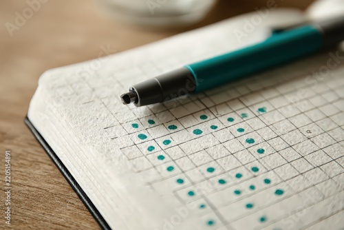 Close-up of a hand-drawn habit tracker grid with teal dots on textured paper beside a pen, with a clean uncluttered composition