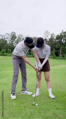 Male golf instructor guiding young Asian woman's grip and swing stance on grass fairway