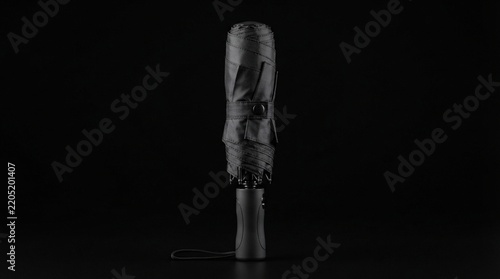 Compact travel umbrella photo, folded black umbrella with ergonomic handle against dark studio background