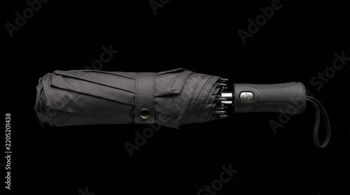 Compact travel umbrella photo, folded black umbrella with ergonomic handle on a black background