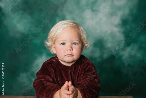 Young child with blonde hair poses calmly in a studio setting