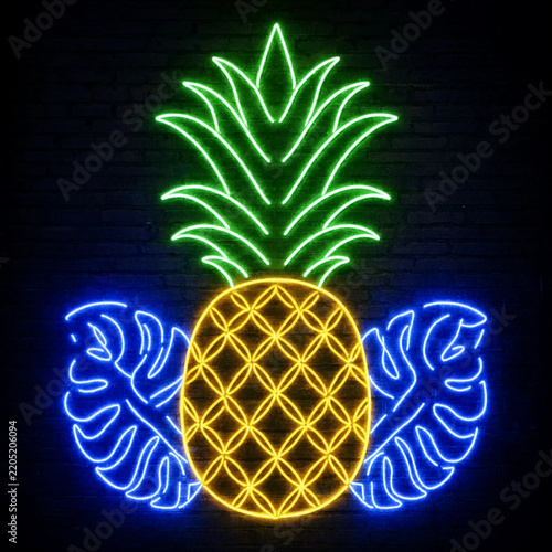 Bright neon sign of a pineapple and tropical leaves glowing on a dark brick wall