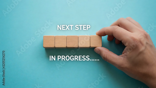Hand placing wooden block with next step and in progress on blue background