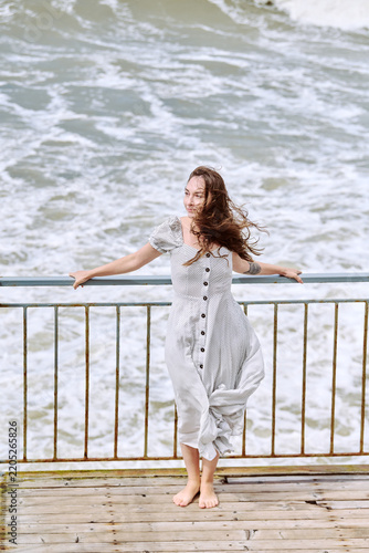 Woman standing beside sea rail in flowing white dress