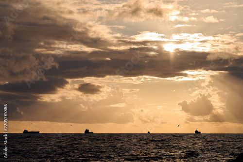 Cargo ships sail across dark ocean beneath golden storm clouds