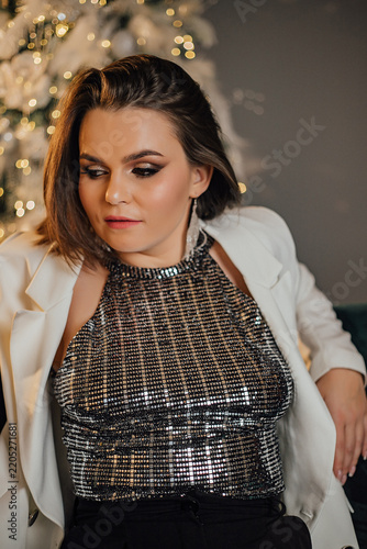 Elegant woman in sequin top and blazer with festive background lighting.