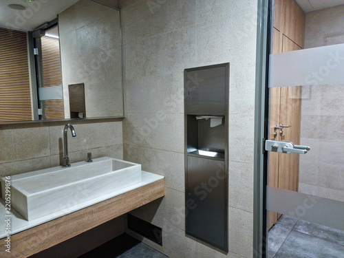 Modern public restroom with rectangular stone basin, wooden vanity, mirror, and built-in steel dispenser