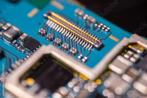 Macro view of blue electronic circuit board with gold connector, microchips, soldered components, and blurred depth of field in a high tech hardware close up