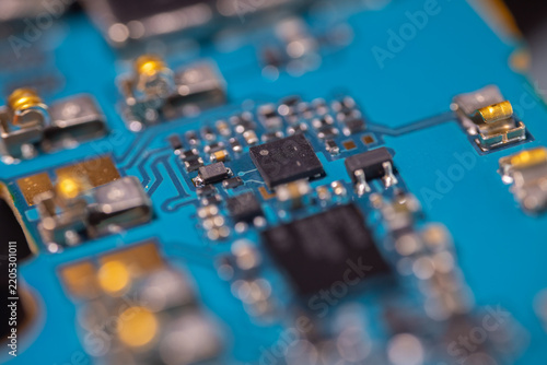 Macro view of blue printed circuit board with black integrated circuits, metallic components, soldered connections, and shallow depth of field in electronics hardware