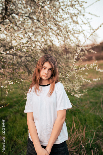 Happy teenage girl in a white T-shirt posing beside a blooming tree, retro film photo with visible grain and noise