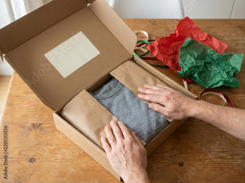 Hands packing a grey sweater into a cardboard box. Person returning a gift after Christmas.