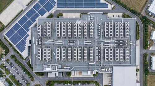 Top-down drone photo of a large data center building featuring rows of rooftop cooling units, solar panels, and surrounding farmland