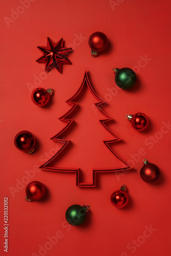 Minimalist Christmas tree outline composition surrounded by red and green ornaments on red background