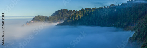 Beautiful wide panoramic view of a historic lighthouse on a misty rocky ocean coast at sunrise