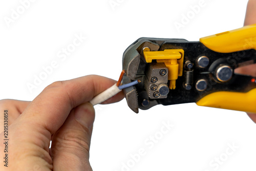 Electrician’s automatic wire stripper with yellow handles removing insulation from a multi‑core cable; hands holding the tool and wire against a clean white background