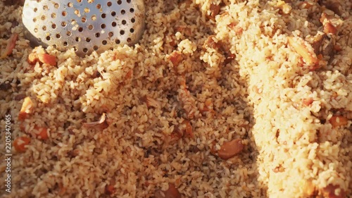 Freshly prepared spiced rice cooks together with juicy meat and chopped carrots. Huge pan holds massive portion of authentic culinary masterpiece ready for eating. plov or biryani