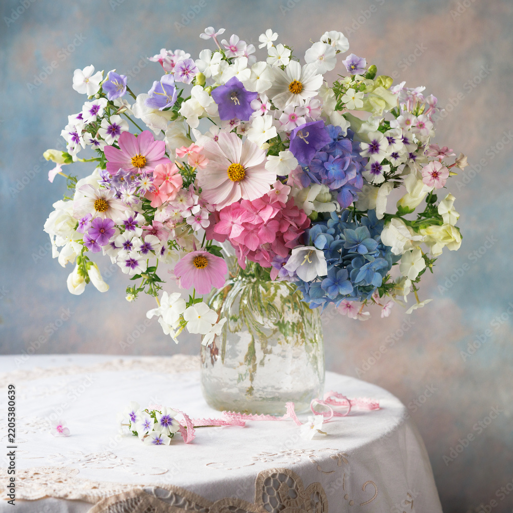 Fototapeta premium Beautiful bouquet of phlox, cosmos flower, hydrangeas, and bellflowers in a vase on a table; close-up still life, blur, selective focus.
