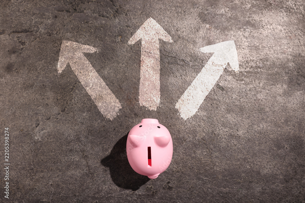 Fototapeta premium Pink piggy bank in front of arrows pointing in different directions on grey stone surface, top view.