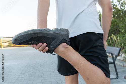 Person warming up, holding foot to stretch leg for fitness. Preparing body for physical activity and exercise