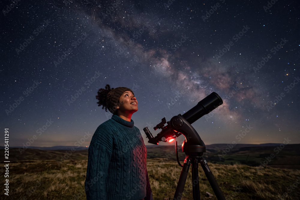 Fototapeta premium Young Black woman looking at starry sky next to telescope