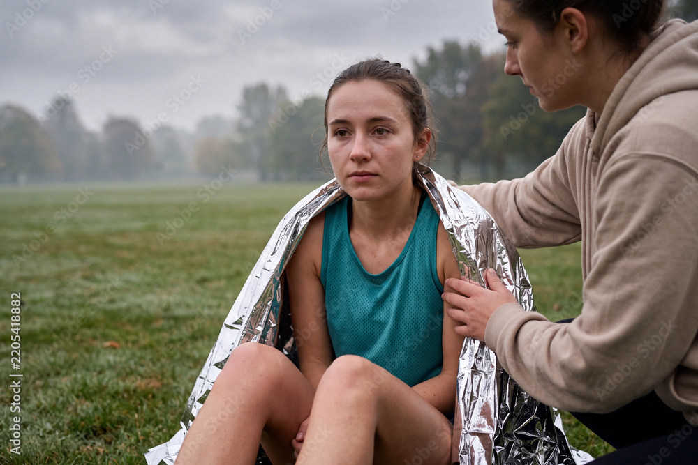 Naklejka premium Woman comforting a disappointed runner wrapped in a foil blanket