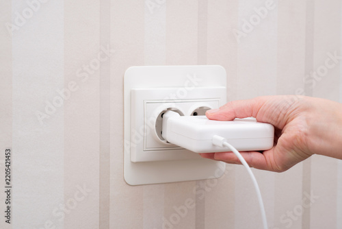 A female hand inserting a white power adapter into a wall outlet while a charging cable is connected