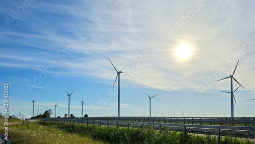 Wind turbines across a green agricultural field beneath blue sky.