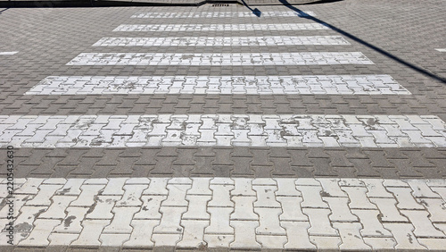 Worn white pedestrian crossing on interlocking gray pavement pattern.
