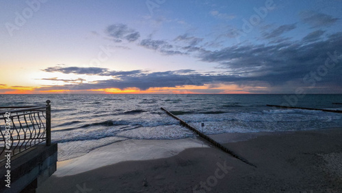 Dramatic Seaside Sunset with Waves, Groynes and Dark Cloudy Sky.