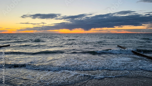 Dramatic Seaside Sunset with Waves, Groynes and Dark Cloudy Sky.