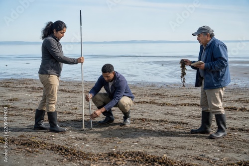 Coastal erosion monitoring scientists aligning tide-reference observations beside a wrack line