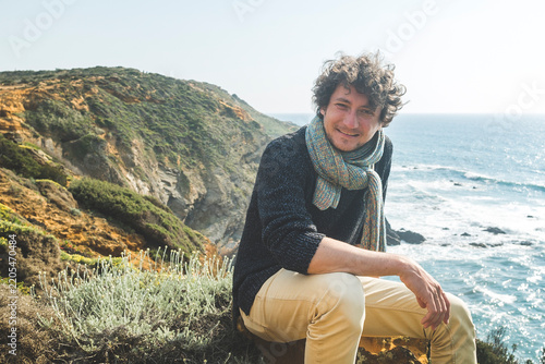 Man with curly hair and scarf sitting on a coastal cliff, Alteirinhos Beach, Zambujeira do Mar, Costa Vicentina, Alentejo, Portugal