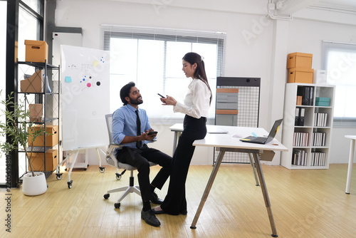 Fotografie Wide shot of young Indian businessman and Asian businesswoman, candid workplace