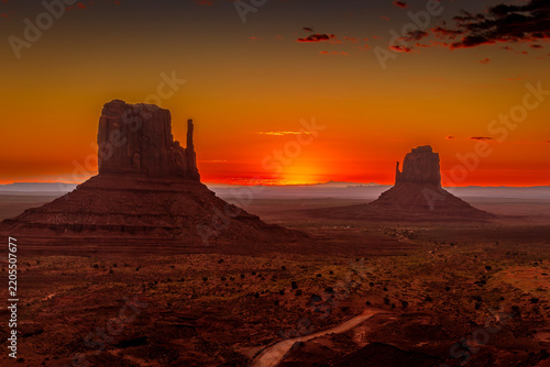 Sun rising on the desert horizon between West Mitten and East Mitten Buttes at sunrise, vibrant orange sky, Monument Valley Tribal Park, USA
