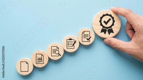 Hand placing a wooden block with a assurance certification on of a rising stack of business process and document workflow symbols