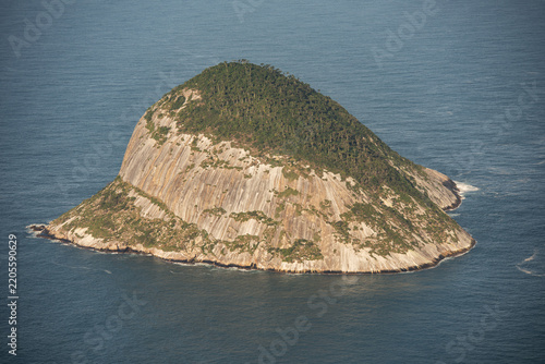 Aerial view of the rocky island of Ilha Rasa rising from the deep blue Atlantic Ocean with steep granite cliffs and lush green vegetation in Rio de Janeiro, Rio de Janeiro, Brazil.