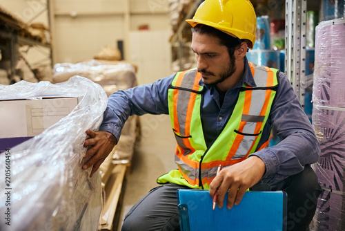 Male worker checking wrapped inventory while working in distribution warehouse.