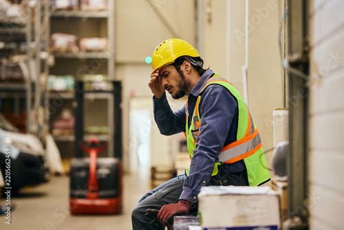 Tired worker with headache resting during shift in distribution warehouse.