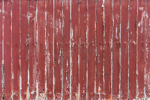 Weathered red painted wooden plank wall texture. Rustic background of vertical wooden planks with faded red paint, peeling surfaces, cracks and distressed details across the full frame.