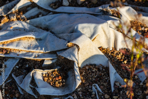 Obraz na plátně Discarded dirty white fabric scraps scattered on the sandy ground, creating a la