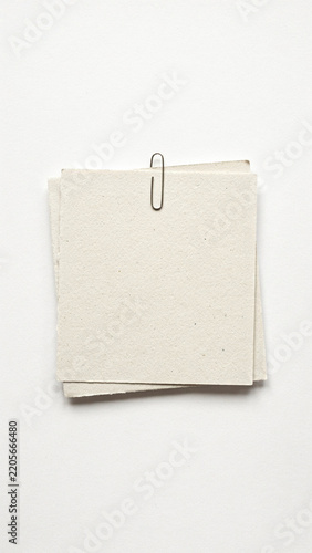 Small pile of textured paper sheets held by metal paperclip with stationery recycled fastener material business background organizer workshop resource template as isolated PNG