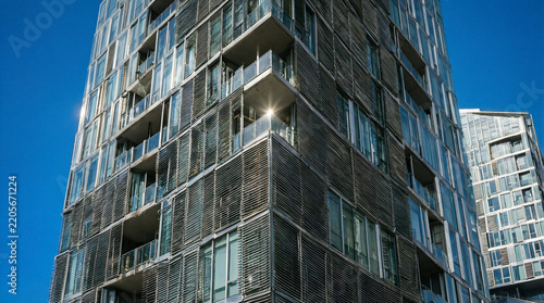 Kinetic facade featuring operable louvers shifting with the sun on a modern glass residential tower against a blue sky